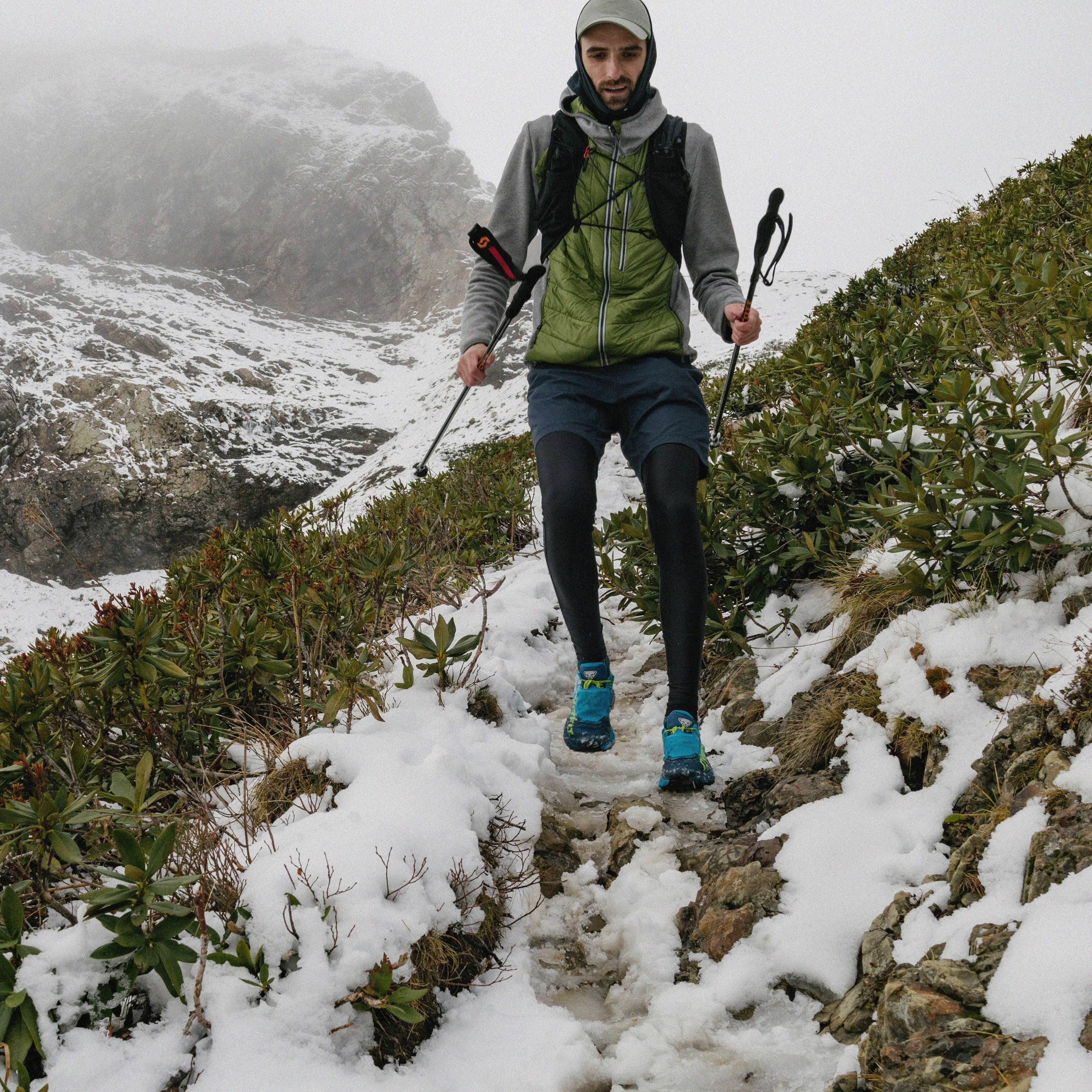 Wanderer mit Trekkingstöcken läuft auf schneebedecktem Bergpfad