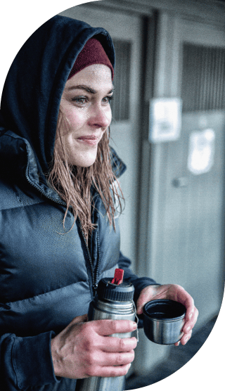 Frau mit nassen Haaren, Mütze und Kapuze hält eine Thermoskanne in der Hand