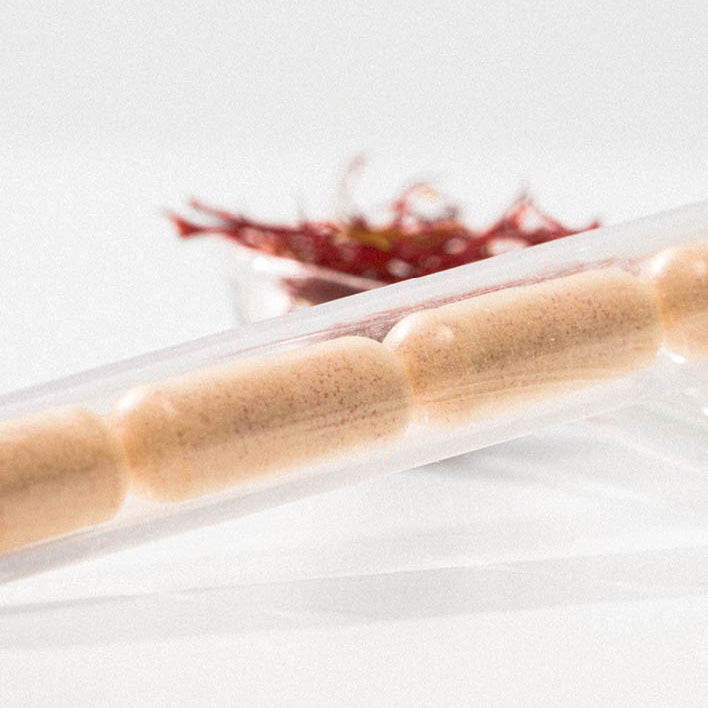 Vier Kapseln in einem transparenten Röhrchen liegen vor einer Schale mit Safranfäden