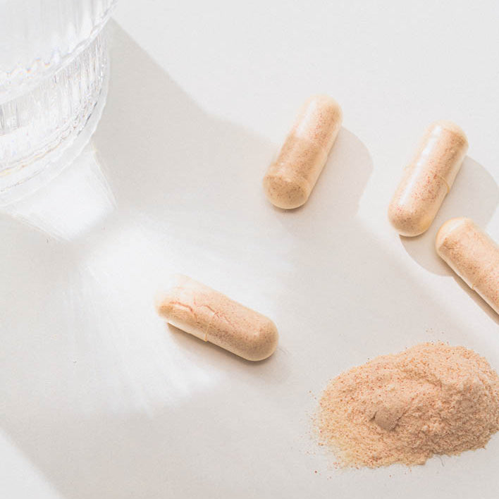 Vier Kapseln neben einem Wasserglas und einem kleinen Haufen Nahrungsergänzungsmittelpulver