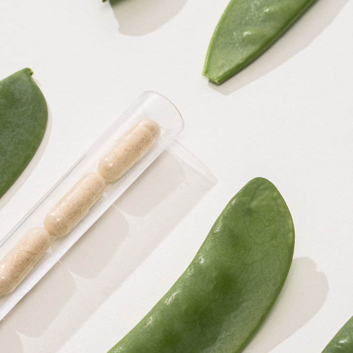 Erbsenschoten und ein Rohr mit Kapseln liegen auf weißem Hintergrund