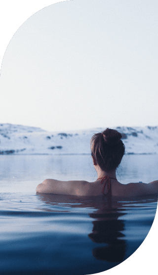 Frau mit Dutt badet in warmen Wasser und schaut auf verschneite Berge