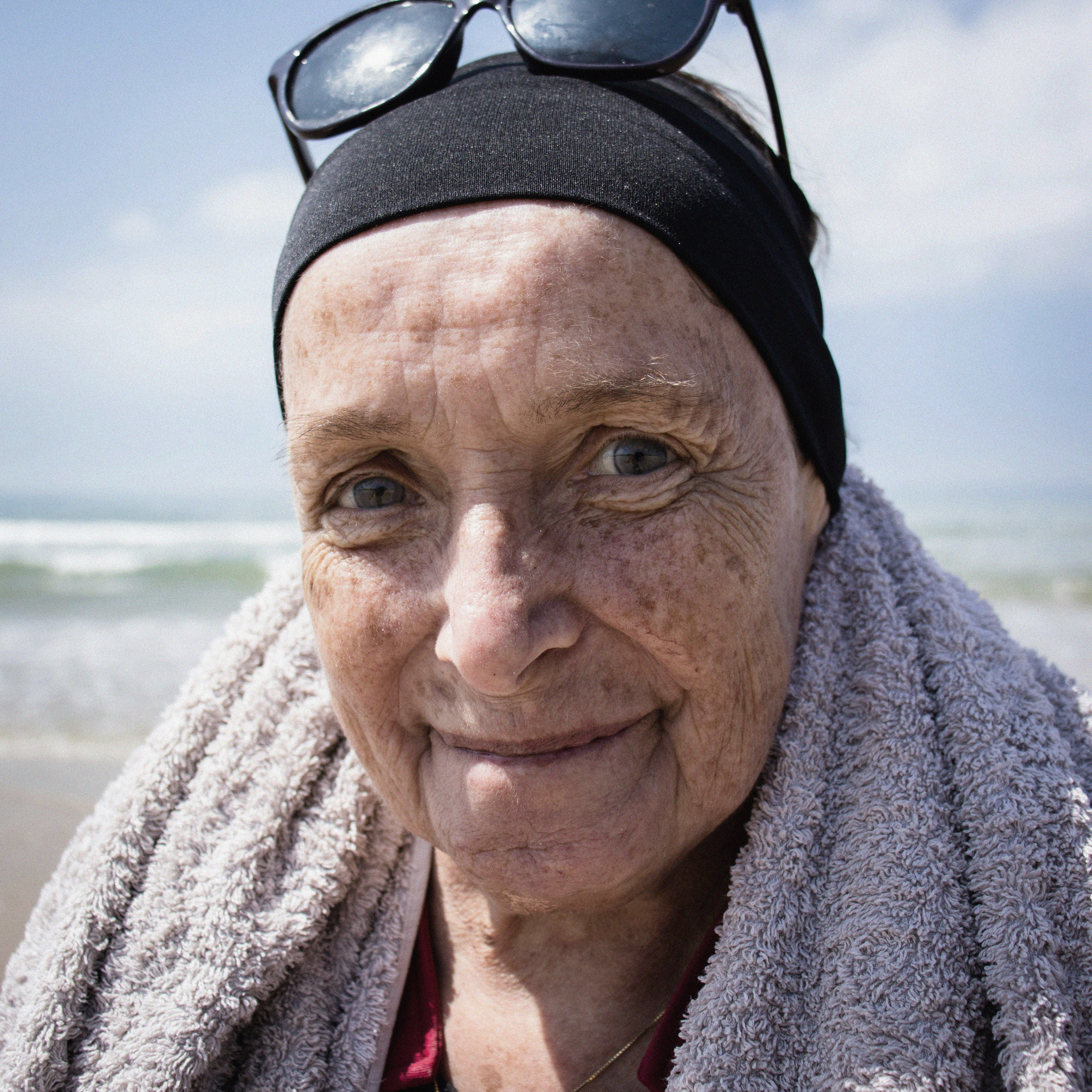 Lächelnde, alte Frau mit Stirnband und Sonnenbrille am Strand