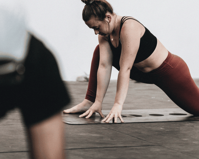 Frau in roter Leggings und schwarzem Top macht Yogaübung auf einer Matte in tiefer Dehnungshaltung