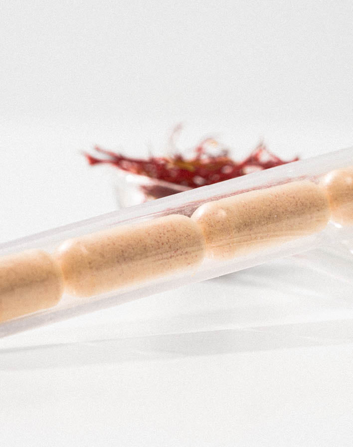 Vier Kapseln in einem transparenten Röhrchen liegen vor einer Schale mit Safranfäden