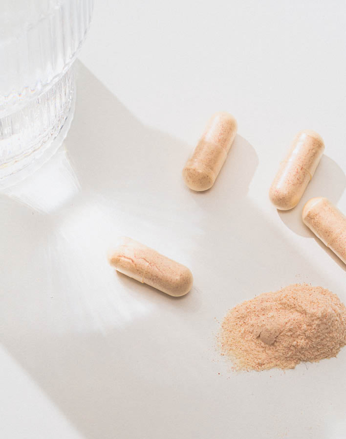 Vier Kapseln neben einem Wasserglas und einem kleinen Haufen Nahrungsergänzungsmittelpulver