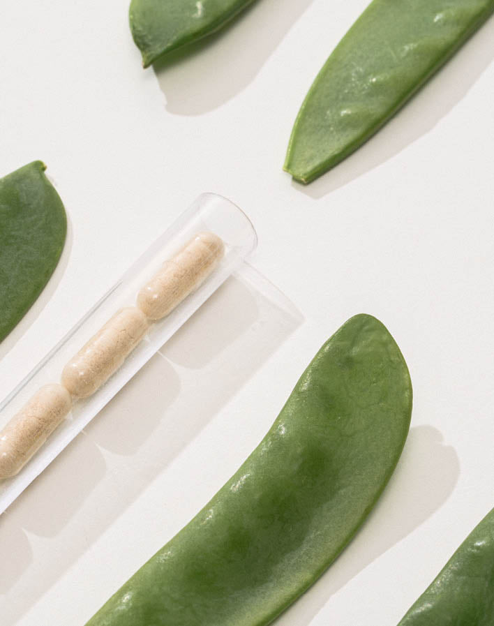 Erbsenschoten und ein Rohr mit Kapseln liegen auf weißem Hintergrund